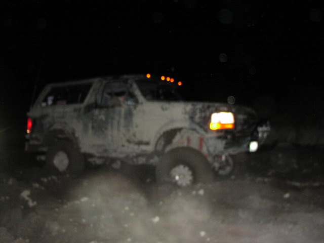 Ford Bronco driving off-road at night, covered in mud