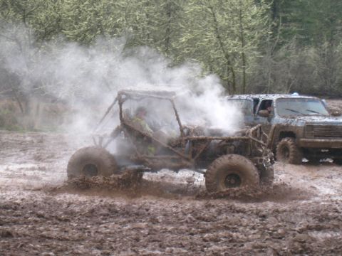 1978 Ford Bronco - Two off-road vehicles are navigating a muddy terrain, with one creating a large cloud of steam or dust.