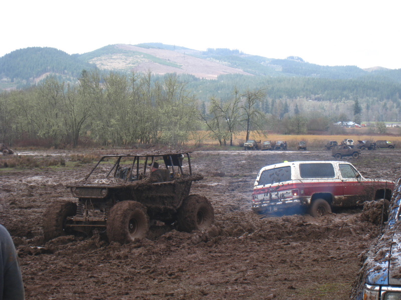 Red and white SUV stuck in mud, with a custom off-road buggy nearby