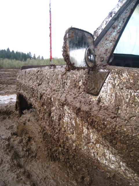 1978 Ford Bronco - A vehicle is heavily covered in mud, with only a partial view of its fender and side mirror visible.