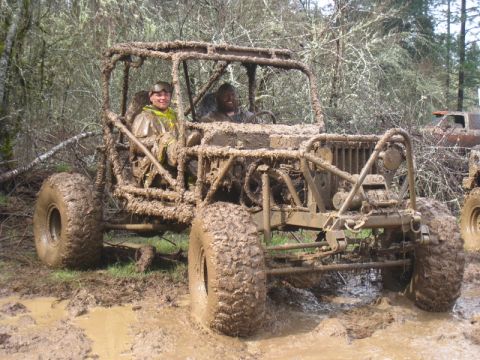 1978 Ford Bronco - Two individuals navigate a heavily mud-covered off-road buggy through a wooded, muddy terrain.