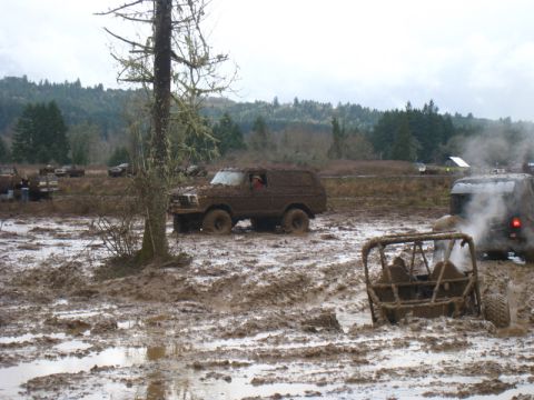 1978 Ford Bronco - Several off-road vehicles are stuck in deep mud under an overcast sky.