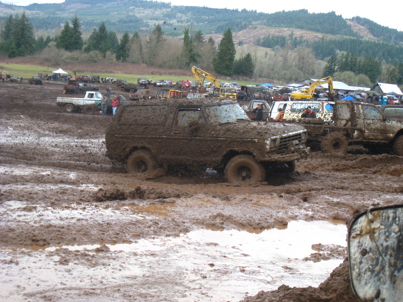1978 Ford Bronco stuck deep in mud, other vehicles and trees in background