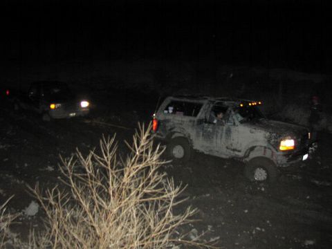 1981 Ford Bronco - Two vehicles are stuck in the mud at night, with one being towed by the other.