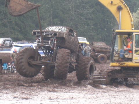 1978 Ford Bronco - A heavily mud-covered 1978 Ford Bronco monster truck navigates a muddy terrain, with an excavator nearby.