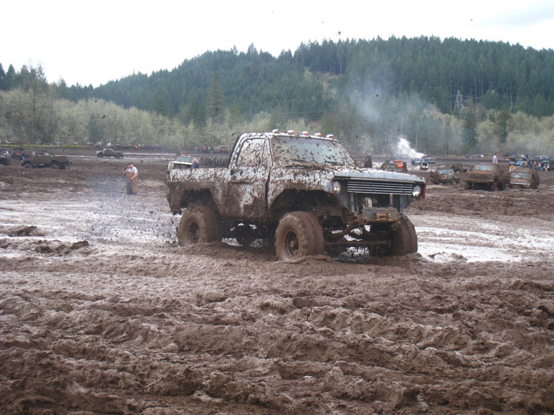 Mud-covered pickup truck stuck in mud pit, other vehicles in background