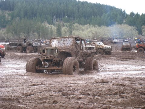 1978 Ford Bronco - Several off-road vehicles are stuck in deep mud during an event, with a forest in the background.