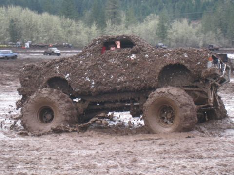 1978 Ford Bronco - A heavily mud-caked off-road vehicle is stuck in a muddy track, with other vehicles in the background.