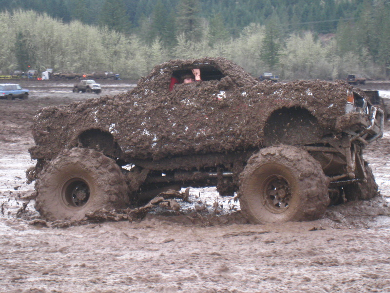Mud-covered off-road vehicle with large tires stuck in mud, driver visible inside