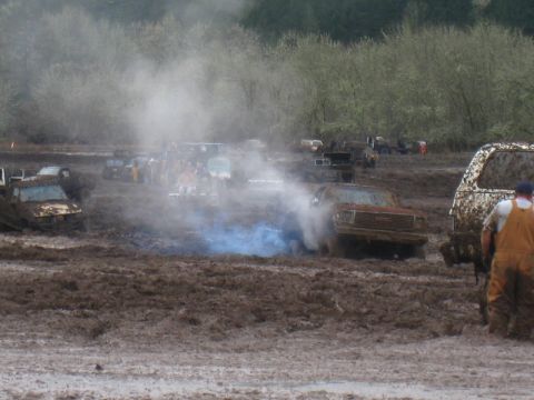 1978 Ford Bronco - Multiple vehicles are stuck in a muddy field during a mud bogging event, with one truck emitting blue smoke.