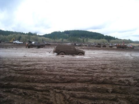 1978 Ford Bronco - Several vehicles are bogged down in a muddy field under an overcast sky.