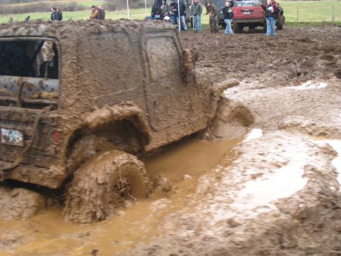 1978 Ford Bronco - An off-road vehicle is deeply stuck in a mud pit during an event, with spectators watching from the side.