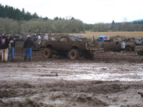 1978 Ford Bronco - Multiple off-road vehicles stuck in deep mud with spectators around.
