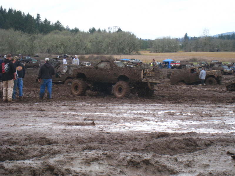 Muddy off-road vehicles and people gathered in a muddy field