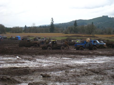 1978 Ford Bronco - Multiple off-road vehicles are bogged down in deep mud under an overcast sky.