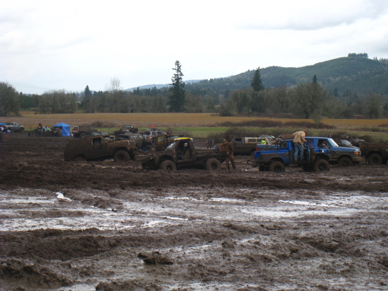 Several trucks and SUVs stuck in a muddy field with trees and hills in the background
