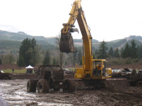 1978 Ford Bronco - An excavator lifts a mud-caked vehicle from a muddy terrain during an event.