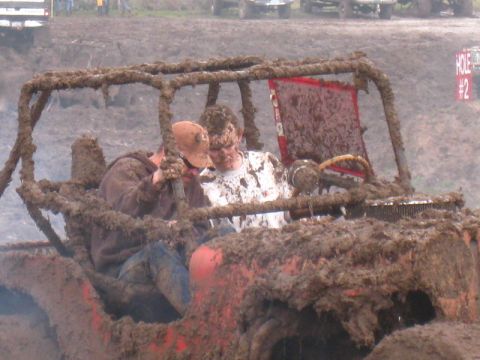 1978 Ford Bronco - Two people are covered in mud while inside a heavily mud-caked vehicle during an off-road event.