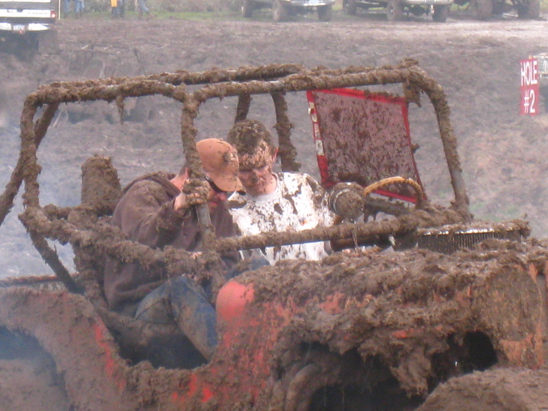 Mud-covered buggy with two guys inside, steering wheel visible