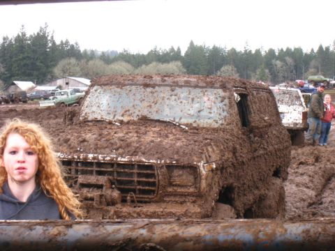 1978 Ford Bronco - A heavily mud-caked van is stuck in a muddy field, with a young person in the foreground.