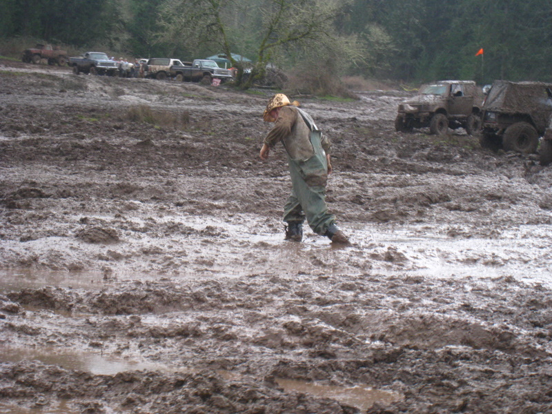 Person walking through mud with several off-road vehicles in the background