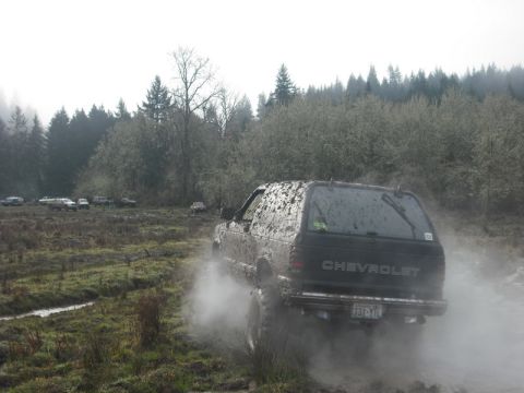 1978 Ford Bronco - A Chevrolet SUV navigates a muddy off-road course, surrounded by trees and other vehicles.