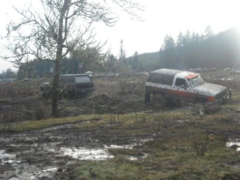 1978 Ford Bronco - Two SUVs are stuck in the mud, one appears to be pulling the other with a rope.