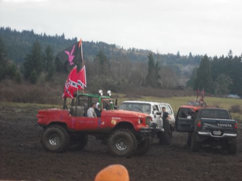 1978 Ford Bronco - Several off-road vehicles are gathered in a muddy area, with trees in the background under an overcast sky.