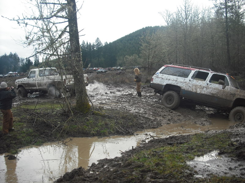 Muddy trucks driving through a wooded area with a stream