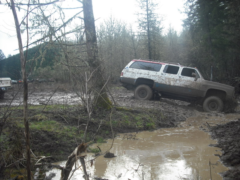 Mud-splattered white and brown SUV with red roof trim navigating a muddy track
