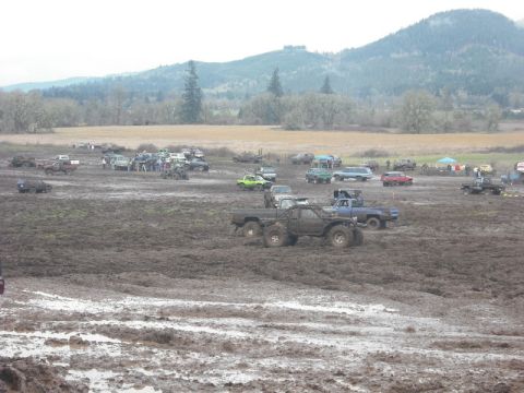 1978 Ford Bronco - Off-road vehicles participating in a mud bog event with spectators and hills in the distance.