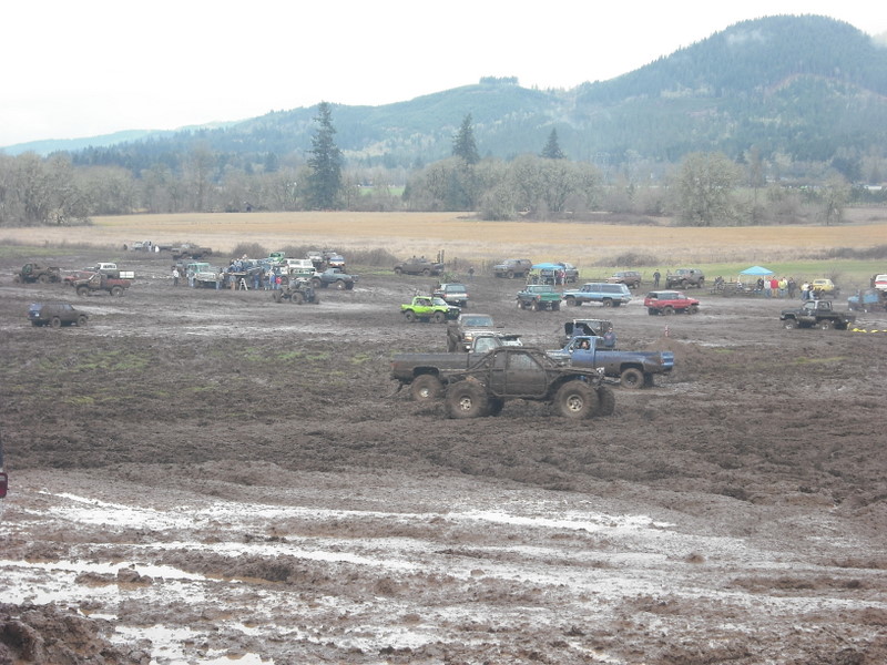 Mud bog event with many trucks and SUVs stuck in the mud, hills in background