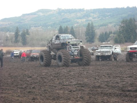 1978 Ford Bronco - Several trucks are stuck in a muddy field with trees and hills in the background.