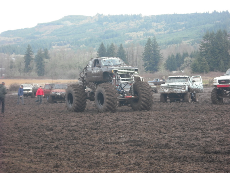 Monster truck with oversized tires in mud, other trucks visible in background