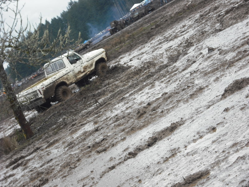White 1978 Ford Bronco driving up a muddy hill, covered in mud
