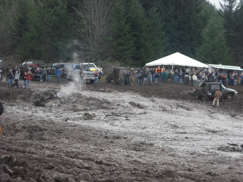 Mud bog scene with off-road vehicles stuck in mud and spectators gathered