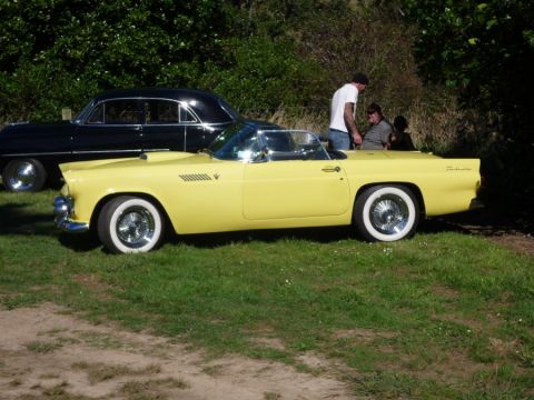 1969 Lincoln Continental - A yellow 1956 Ford Thunderbird convertible is parked next to a black sedan.