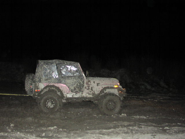 Muddy Jeep with soft top at night, looks stuck