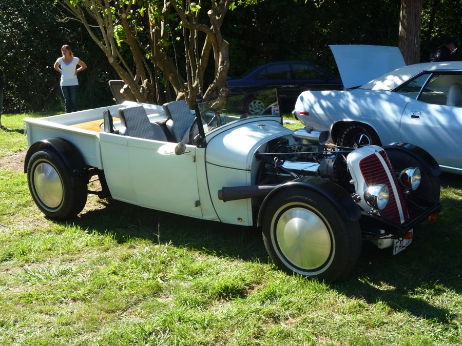 Pale blue hot rod roadster pickup with exposed engine and red grille shell at a grass car show