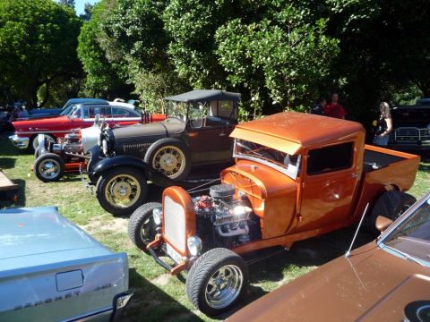 1969 Lincoln Continental - An orange hot rod pickup truck is parked among other classic vehicles at an outdoor gathering.