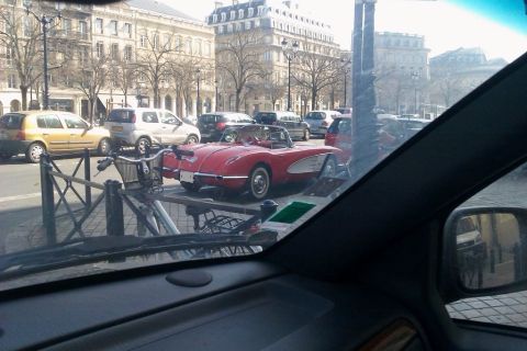1991 Ford LTD Crown Victoria - Shot through a car windshield in a European city square, a red C1 Chevrolet Corvette convertible with white side coves, chrome bumper and w…