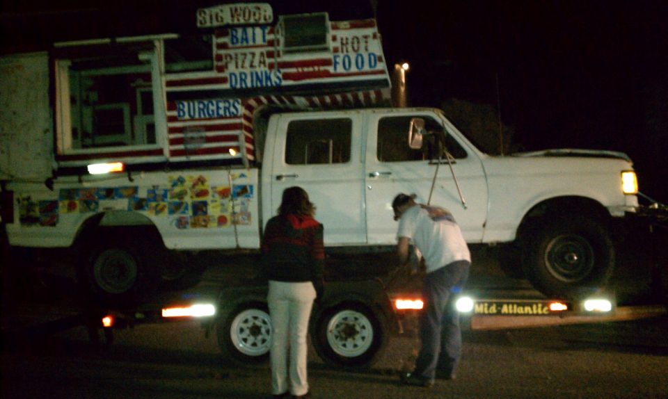 White food truck with 'BIG WOOD BAIT PIZZA DRINKS BURGERS HOT FOOD' signage, on a trailer at night