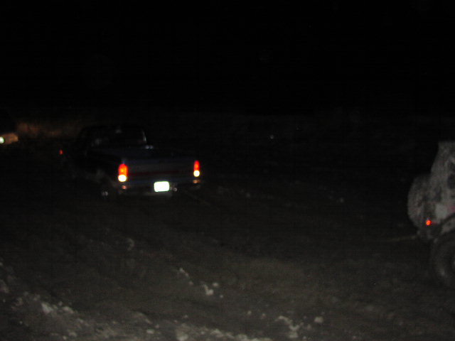 Dark pickup truck with illuminated taillights driving on a dirt road at night