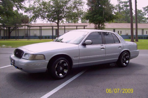 1998 Ford Crown Victoria sedan, silver, parked in a lot with a building in the background