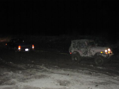 1981 Ford Bronco - Two vehicles are being towed at night, with the lead vehicle's taillights visible and the rear vehicle's headlights illuminated.