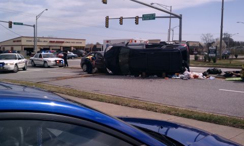 1989 Ford Bronco - An overturned dark SUV lies on its side following a traffic accident, with emergency services on the scene.