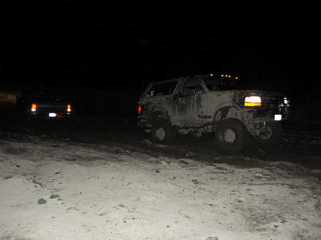 Mud-covered 1992 Ford Bronco with amber marker lights and roof lights, viewed from the front-right at night