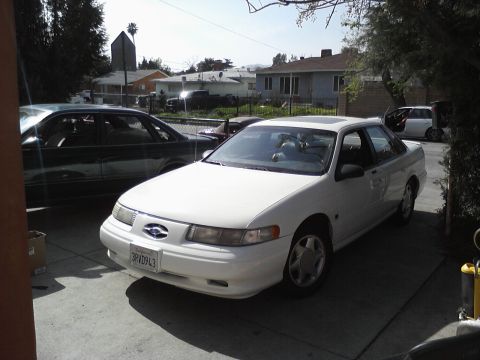 1995 Ford Taurus - A white 1995 Ford Taurus sedan is parked in a driveway next to a dark sedan.