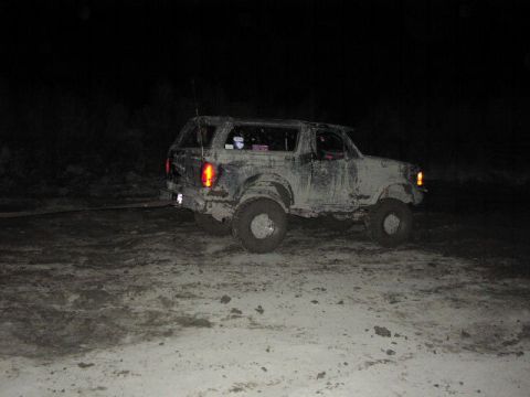 1981 Ford Bronco - Mud-covered SUV being towed at night, with visible tow strap attached to the rear.