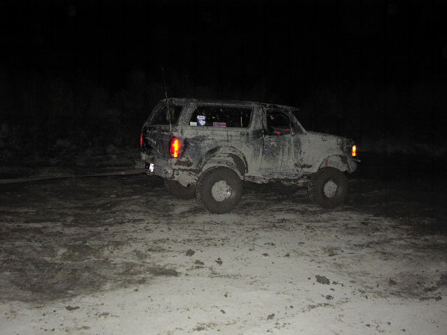 Mud-covered SUV, likely a 1980s Ford Bronco, being towed at night